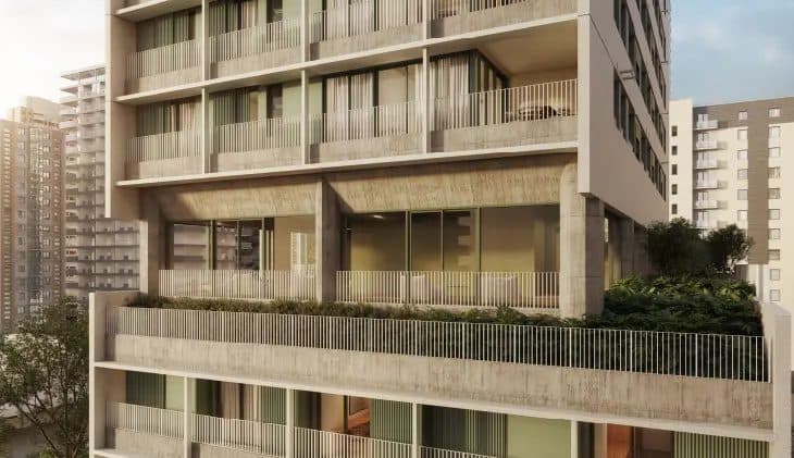 Vista externa de fachada de edifício com varandas e vegetação em nível intermediário.
